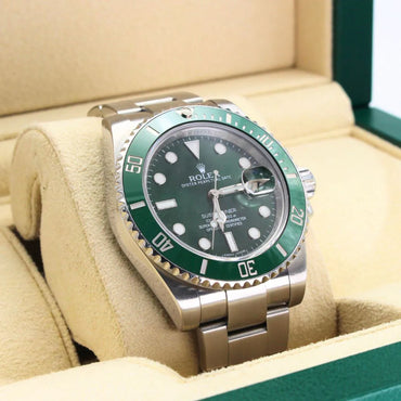 Rolex watch with green bezel and face on a beige cushion in a box