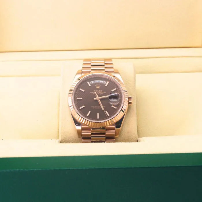 Rolex Day-Date 40 228235 Chocolate Motif Dial 18k Everose Gold Watch Gold wristwatch with a dark face on a green and beige background