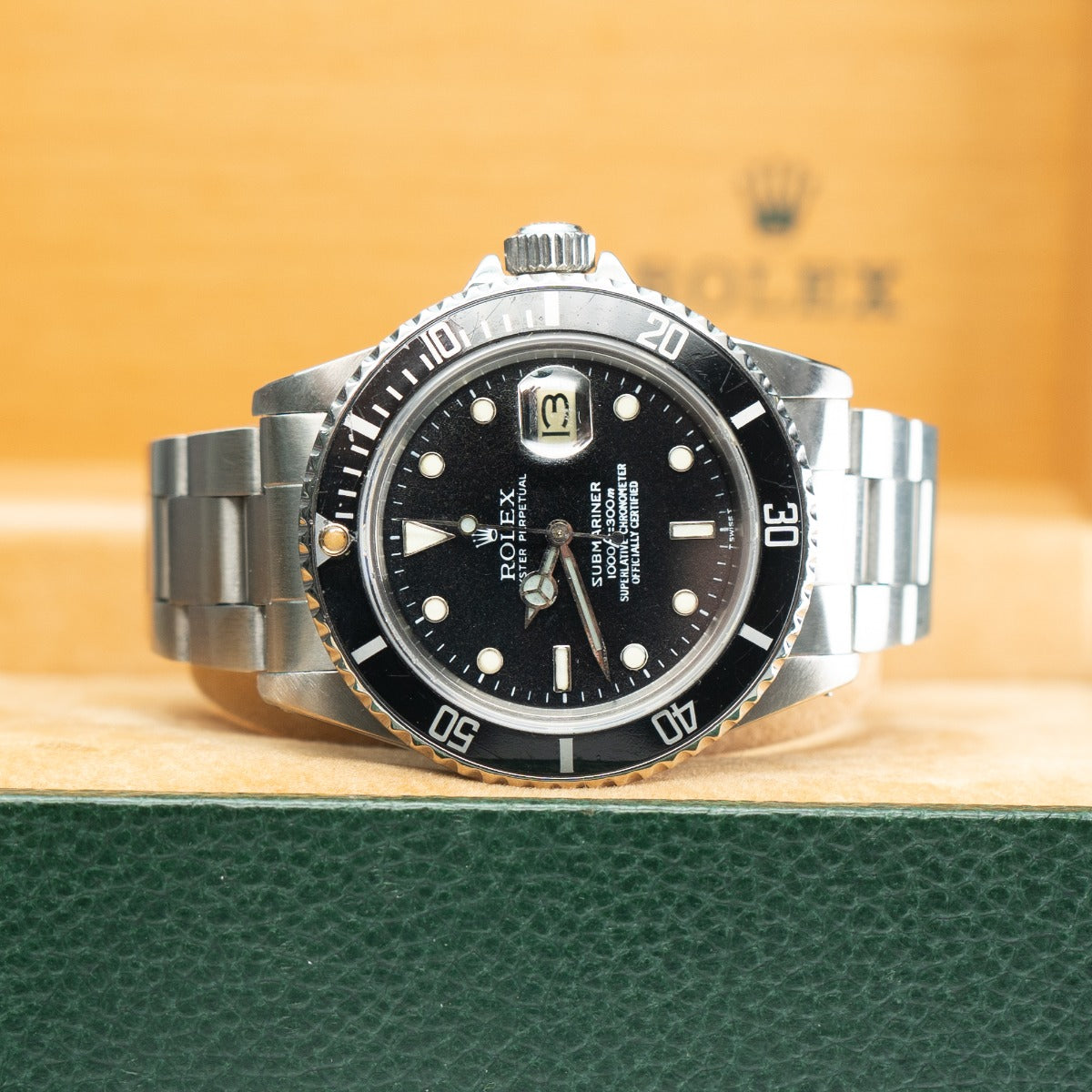 Rolex Submariner 16800 Watch Silver and black watch on a green surface with a blurred background